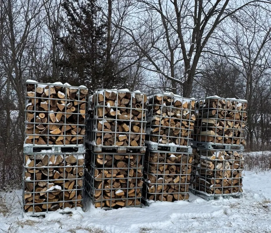 Crates of seasoned split firewood stacked outdoors in winter, ready for delivery or pickup